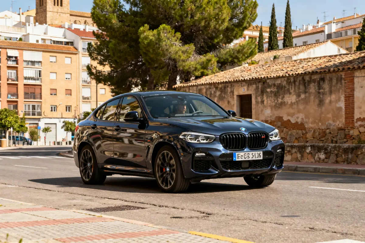 Coche BMW X4 modelo 2025 circulando en una calle urbana bajo el sol.
