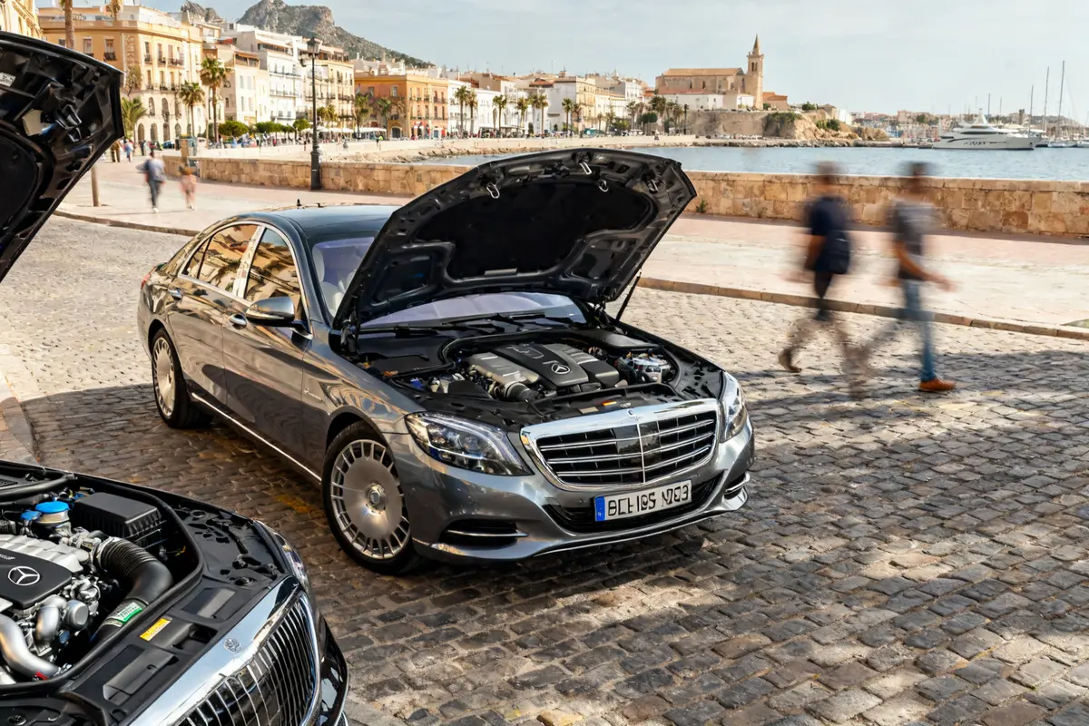 Coche Mercedes W222 gris con capó abierto en un paseo marítimo empedrado.